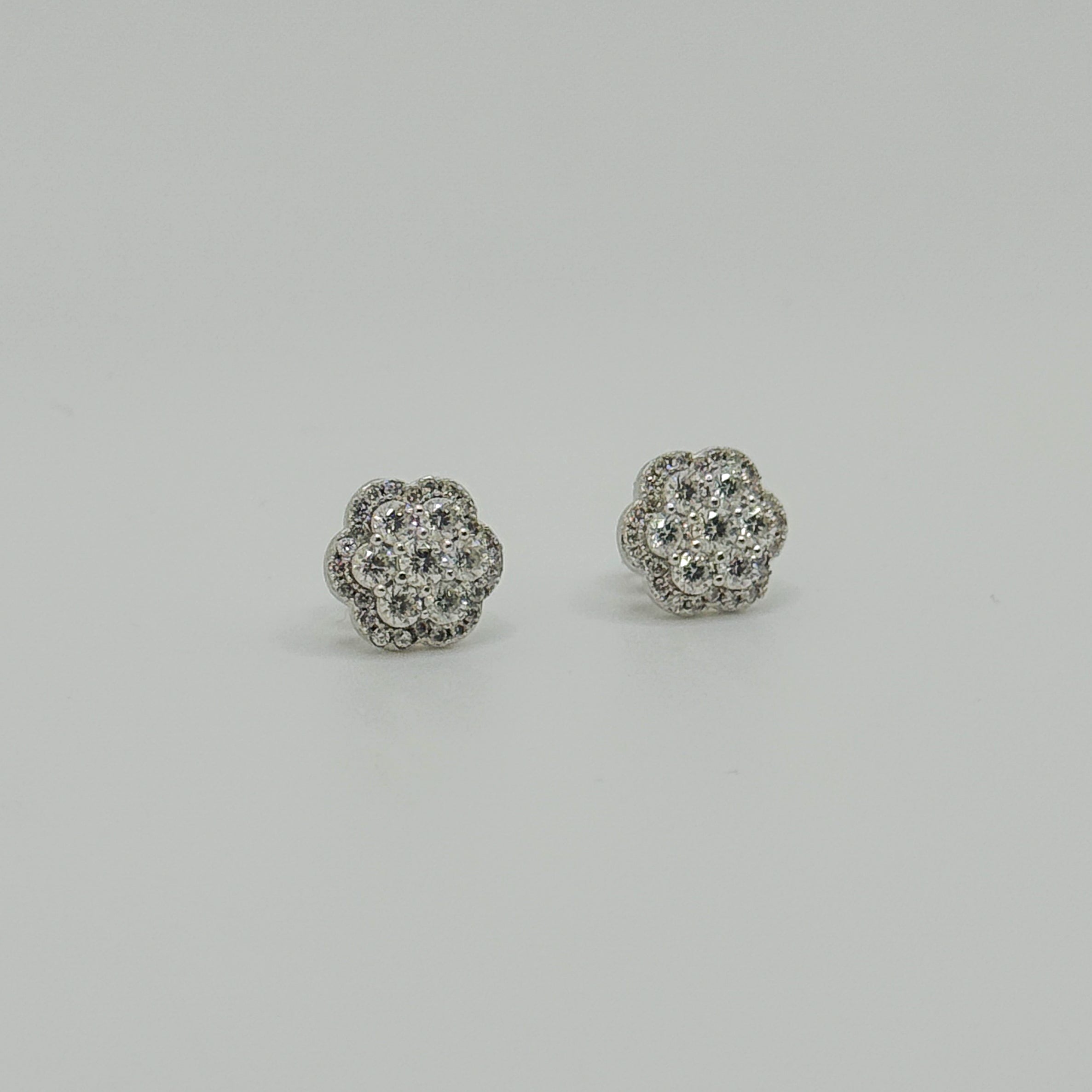A pair of silver-toned stud earrings with a round cluster pavé design set with clear stones, displayed on a neutral light gray background.