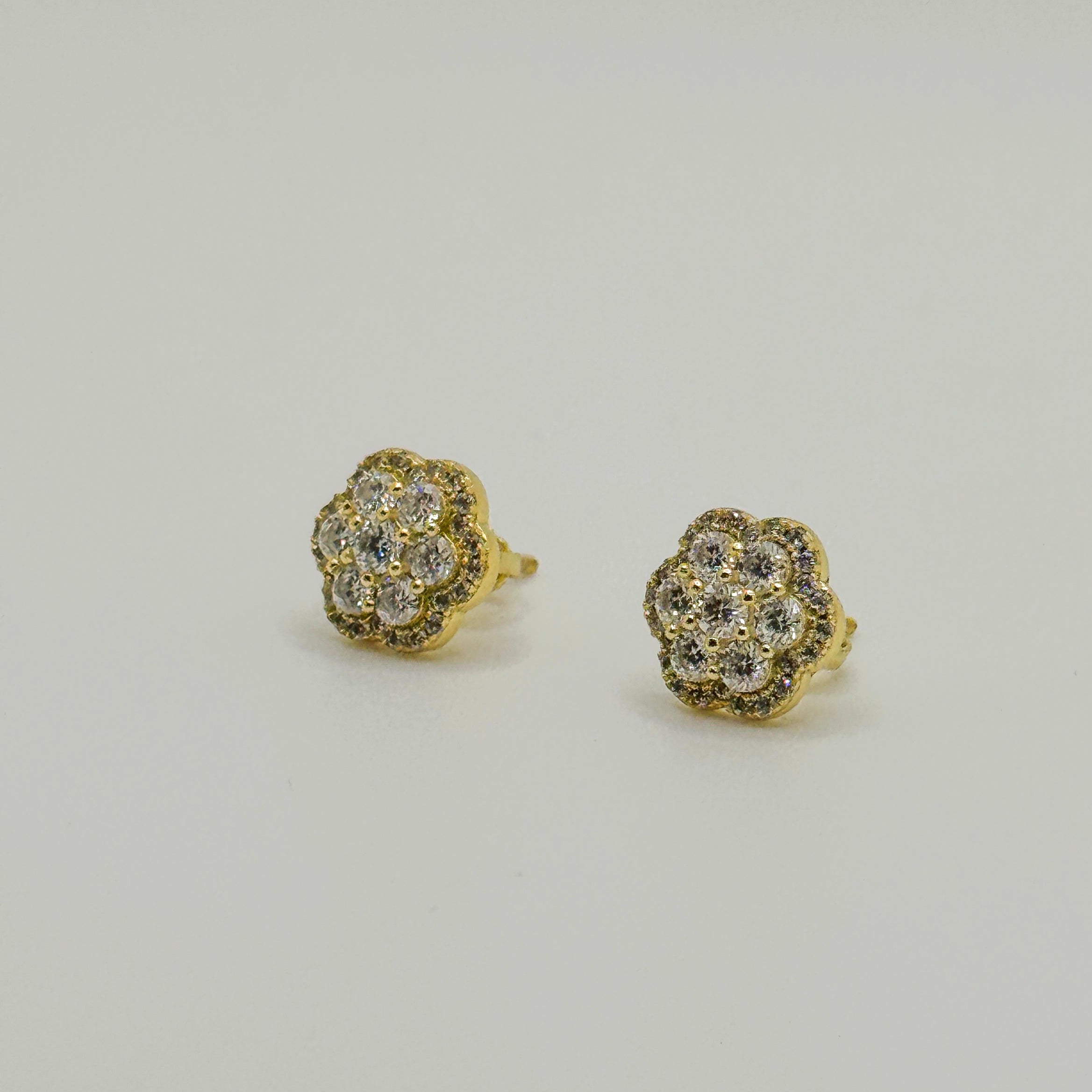 A pair of gold stud earrings with a cluster of clear pavé gemstones, shown on a plain light gray background.