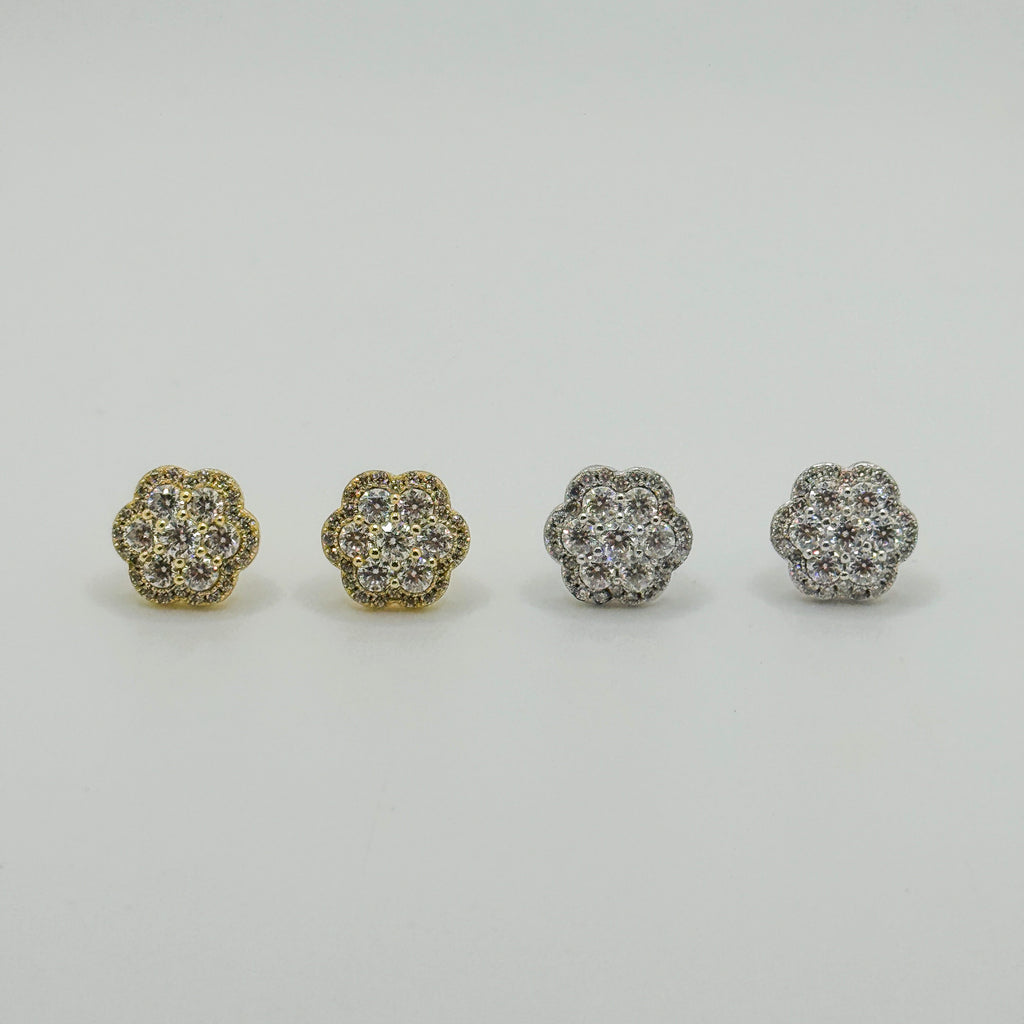 Four small flower-shaped stud earrings arranged in a row on a light gray background. Two earrings are gold-toned and two are silver-toned, each set with clear stones.