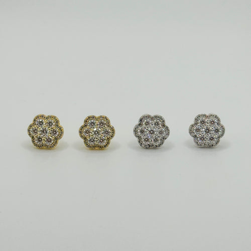 Four small flower-shaped stud earrings arranged in a row on a light gray background. Two earrings are gold-toned and two are silver-toned, each set with clear stones.