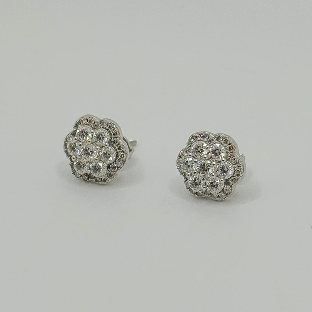 A pair of round flower-shaped stud earrings set with clear pavé gemstones in a silver-toned metal, displayed on a neutral light gray background.