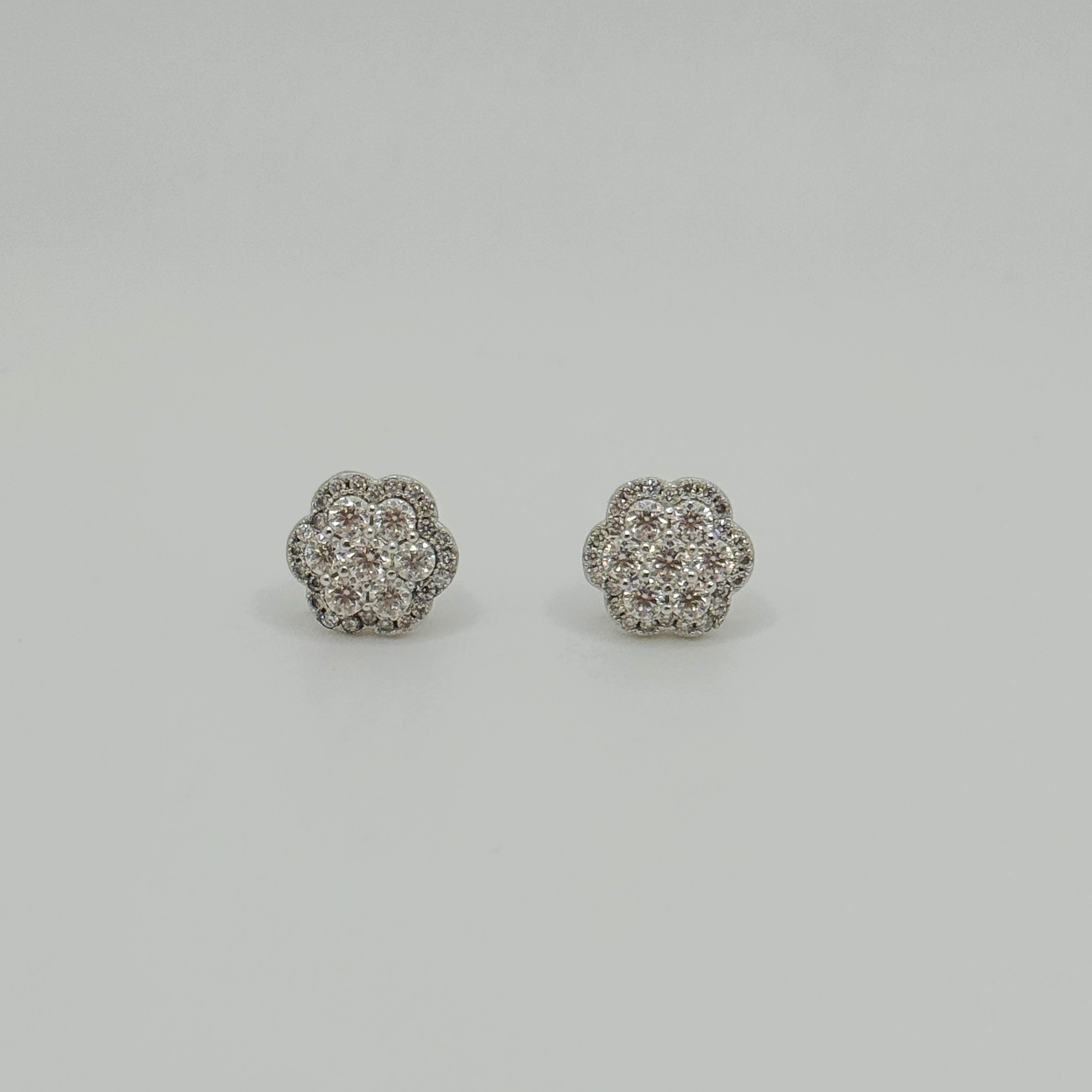 A pair of round flower-shaped stud earrings set with clear pavé gemstones in a silver-toned metal, displayed on a neutral light gray background.