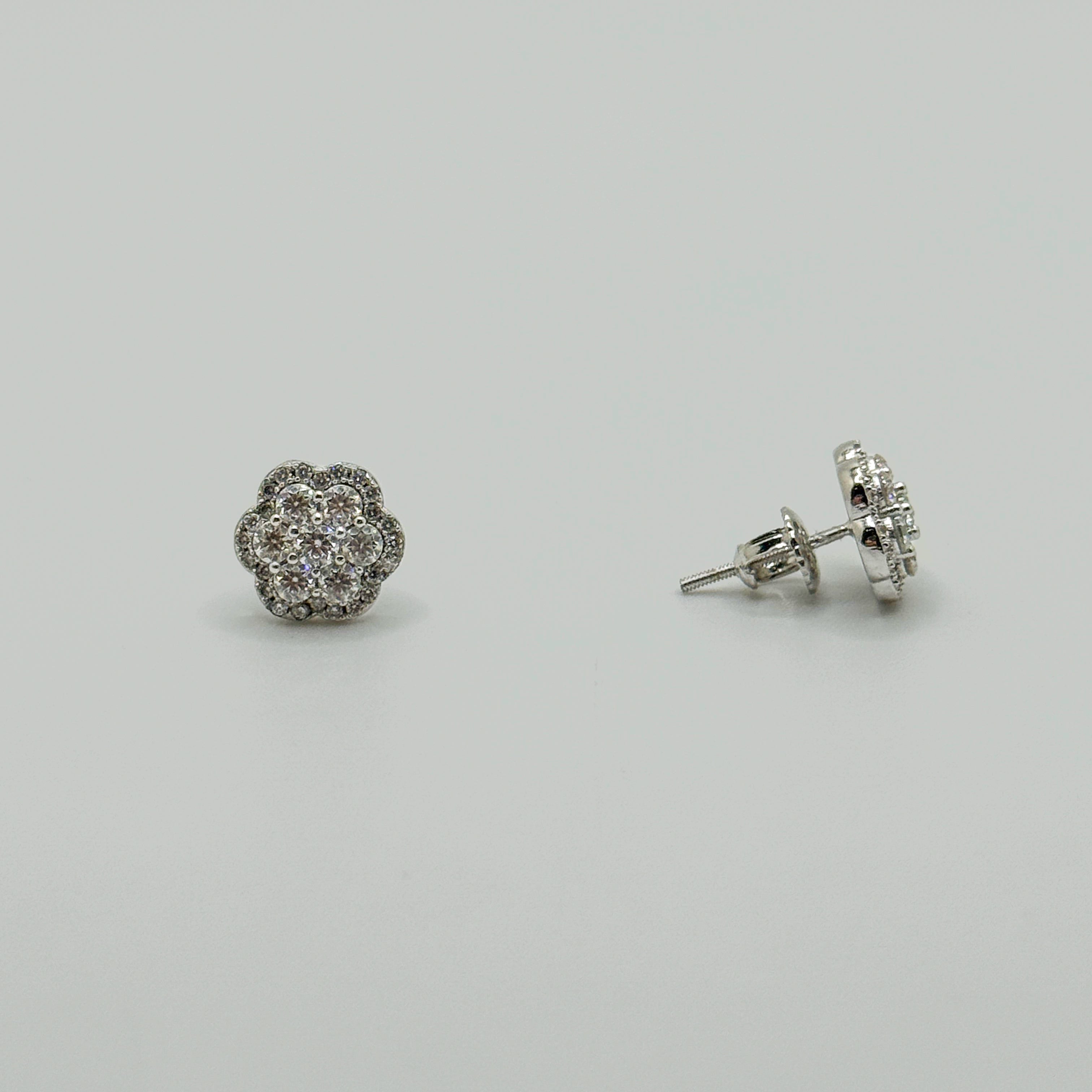 A pair of silver stud earrings with round floral clusters of small clear stones, shown on a plain light gray background. One earring is facing forward and the other is turned to show the post and backing.
