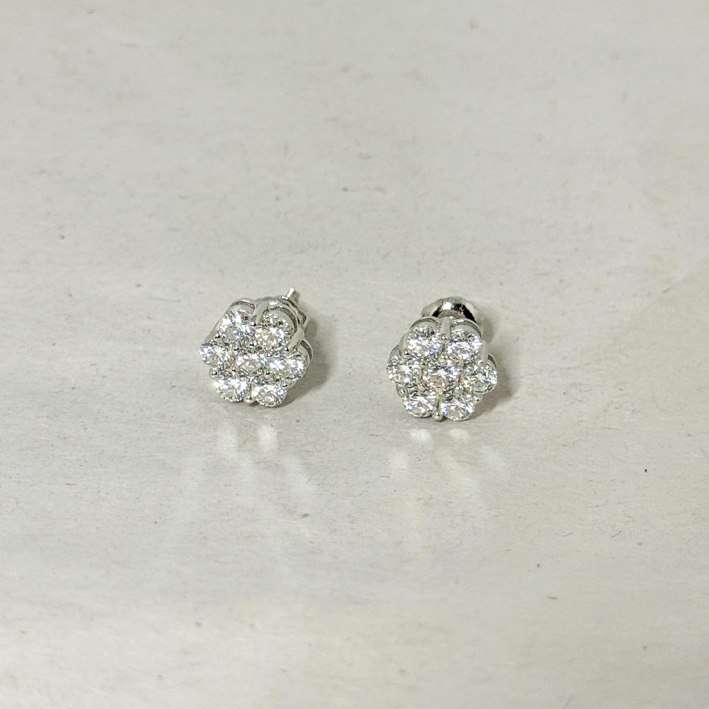 A pair of silver-toned stud earrings with round cluster pavé diamond settings, displayed on a light gray textured surface.