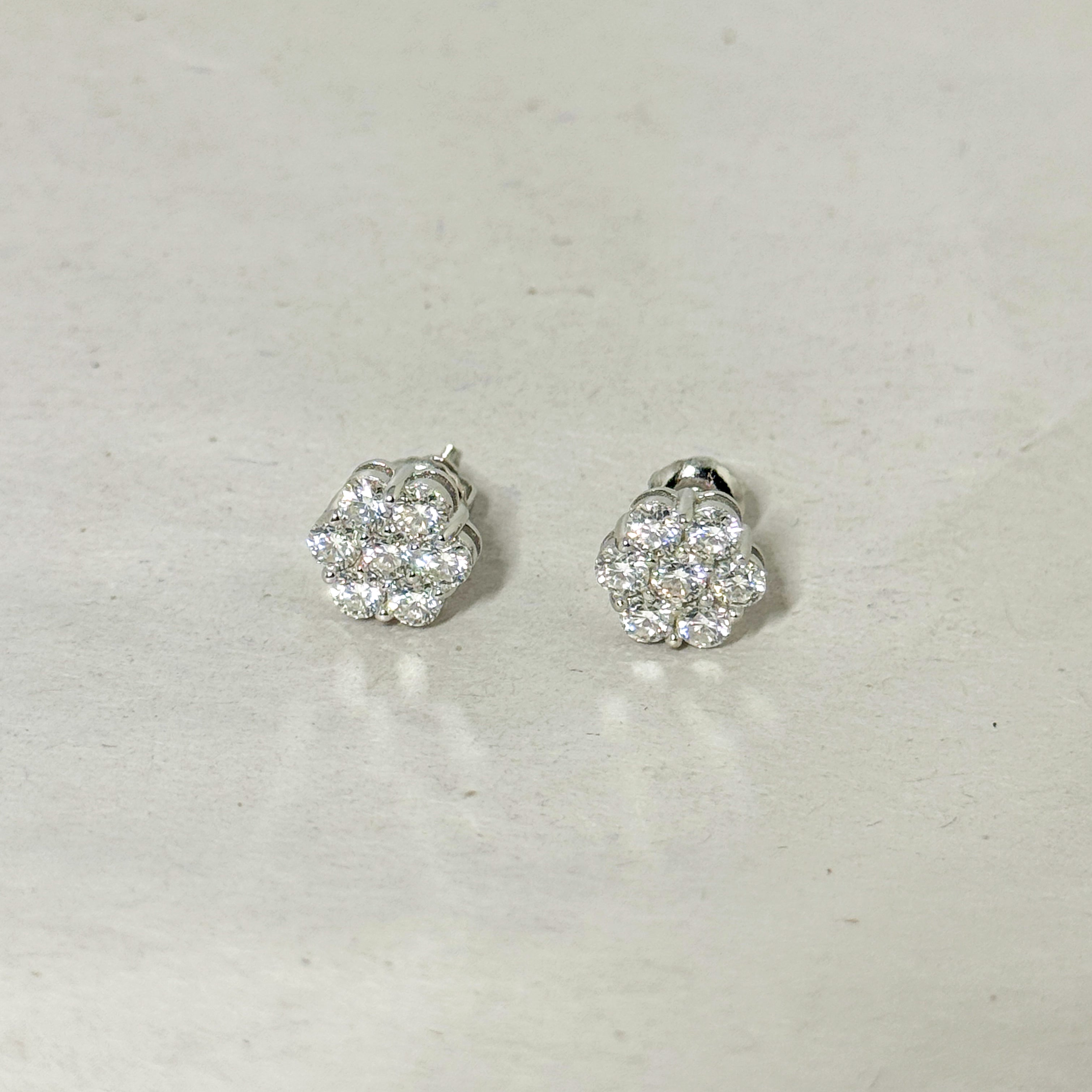 A pair of silver-toned stud earrings with round cluster pavé diamond settings, displayed on a light gray textured surface.