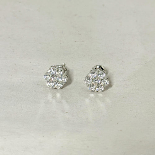 A pair of silver-toned stud earrings with round cluster pavé diamond settings, displayed on a light gray textured surface.