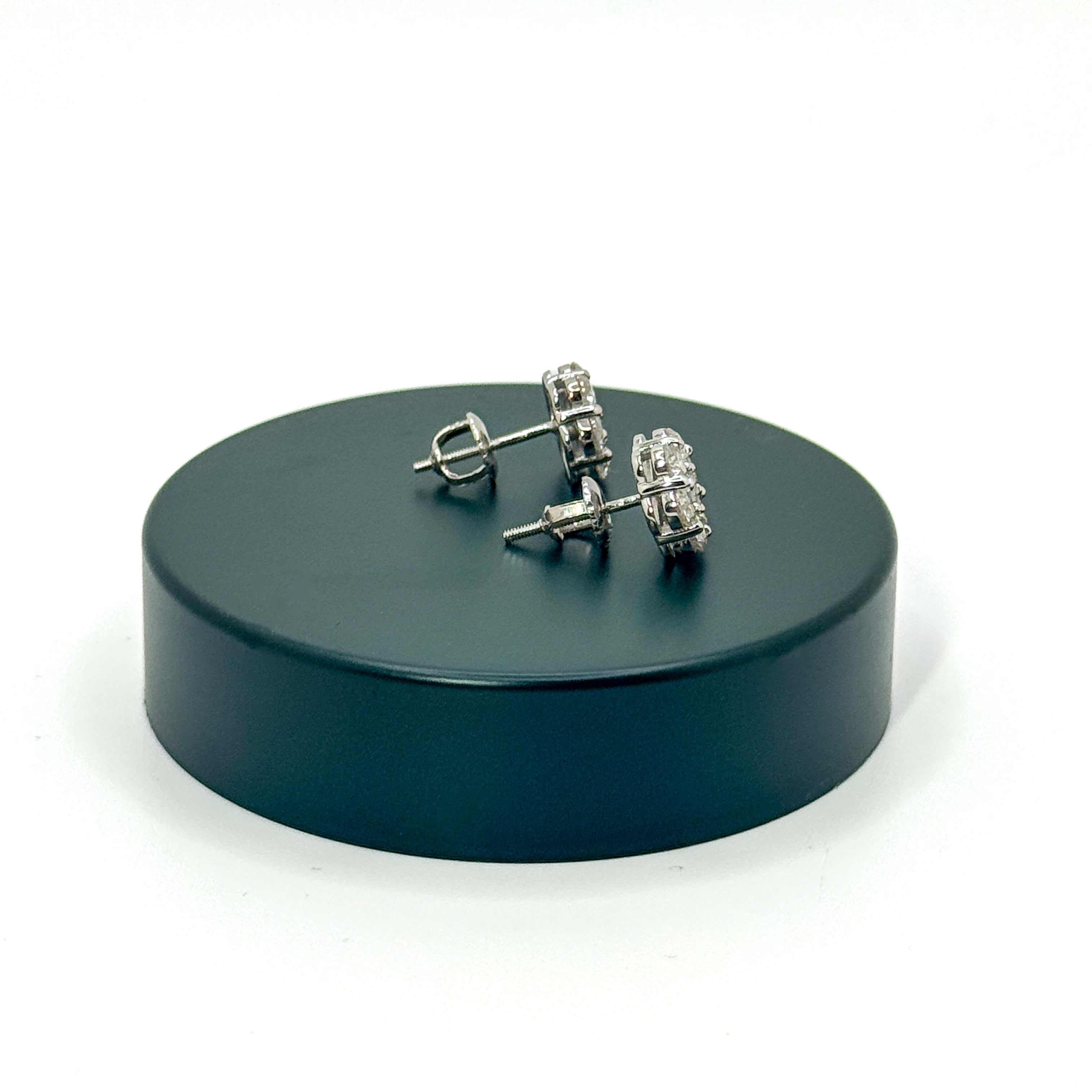 A pair of silver-toned stud earrings with clear gemstones, displayed on a round black stand against a white background.