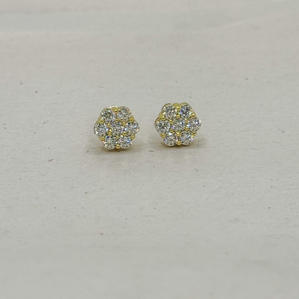 A pair of small gold stud earrings with clear pavé gemstones, arranged on a light beige textured surface.