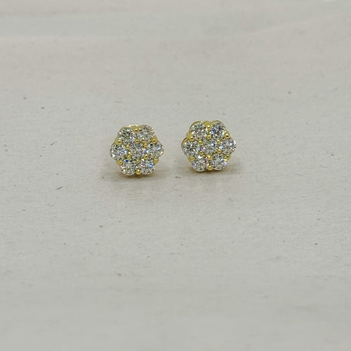A pair of small gold stud earrings with clear pavé gemstones, arranged on a light beige textured surface.