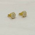 A pair of yellow gold stud earrings with round-cut clear gemstones, displayed on a light beige textured surface.