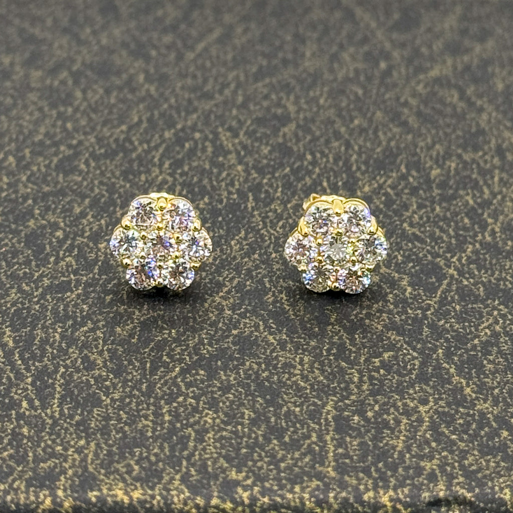 A pair of gold stud earrings with clear pavé gemstones, displayed on a textured dark gray surface.