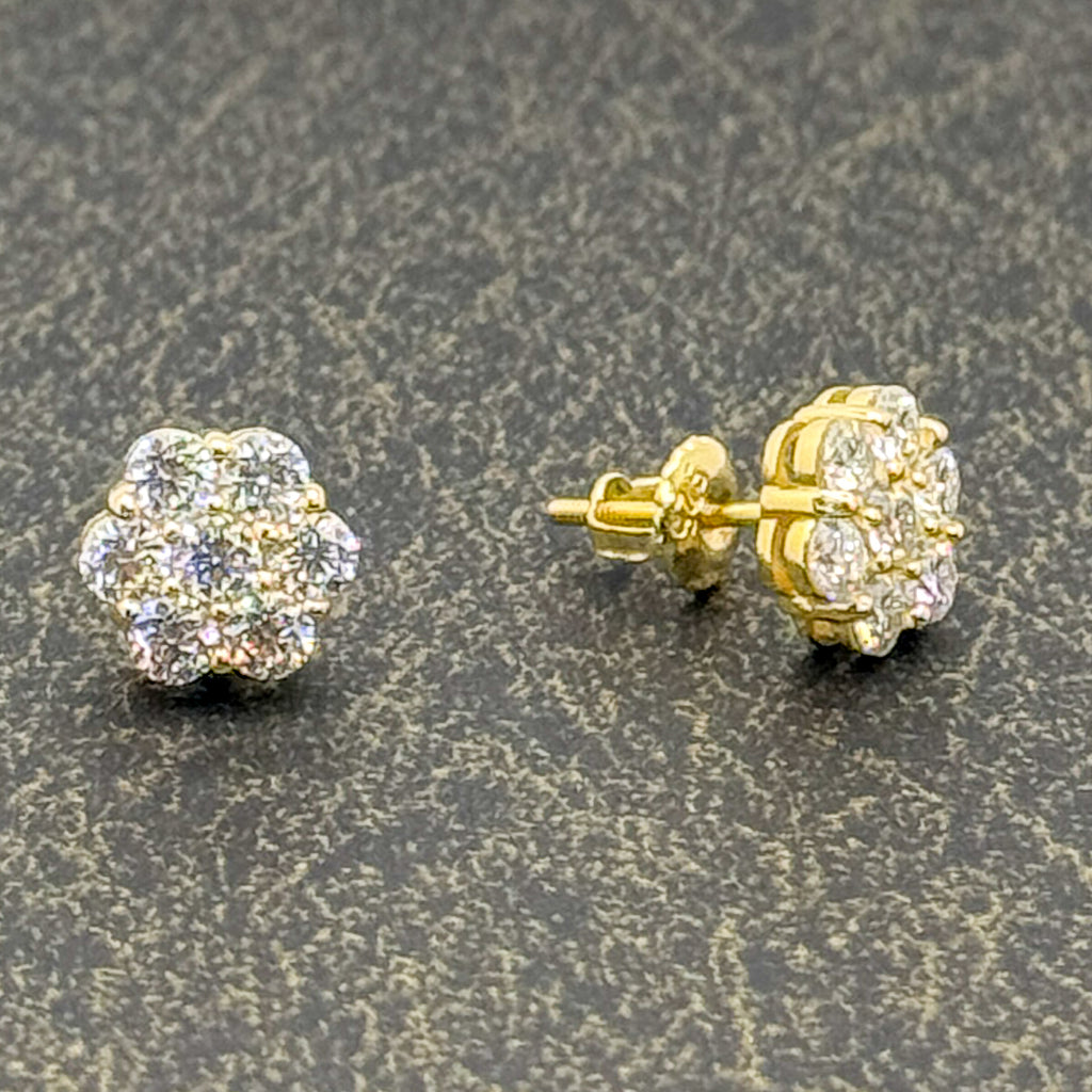 A pair of yellow gold stud earrings with round cluster settings set with clear stones, shown on a textured dark gray background. One earring is facing forward, and the other is turned to show the post and backing.